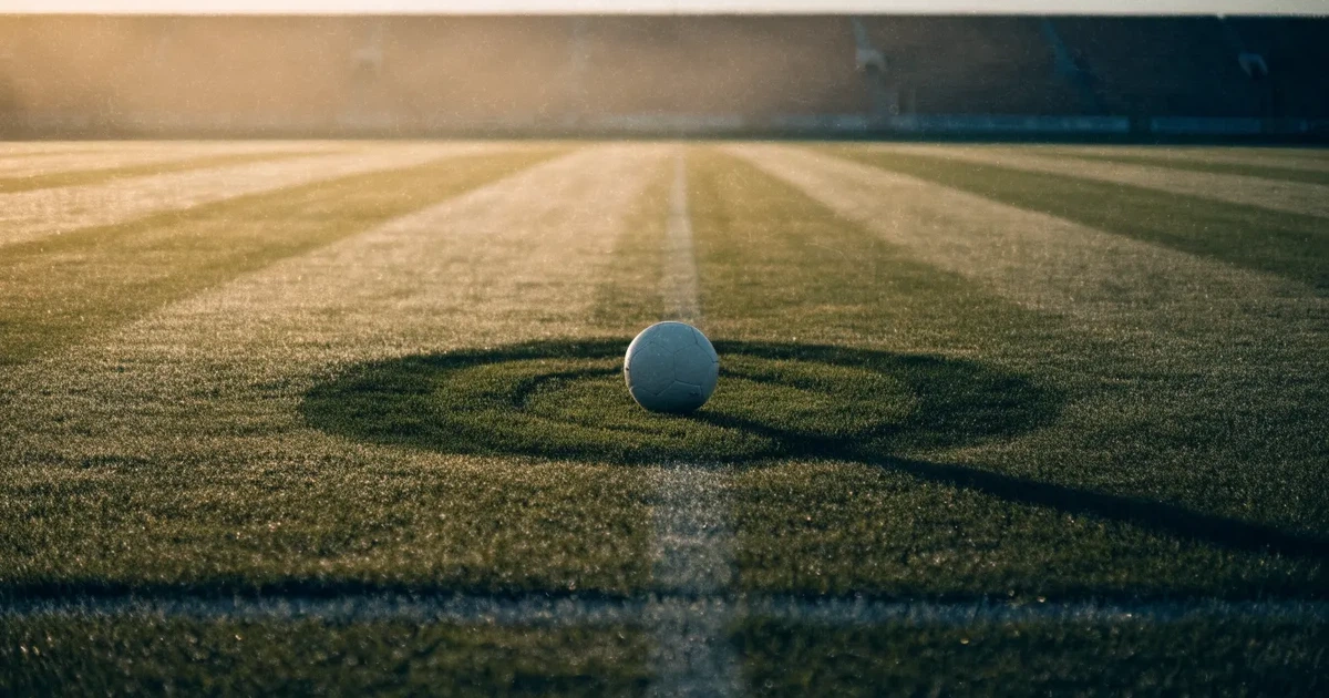 Un pallone da calcio sul dischetto del centrocampo di un prato, alla luce del mattino