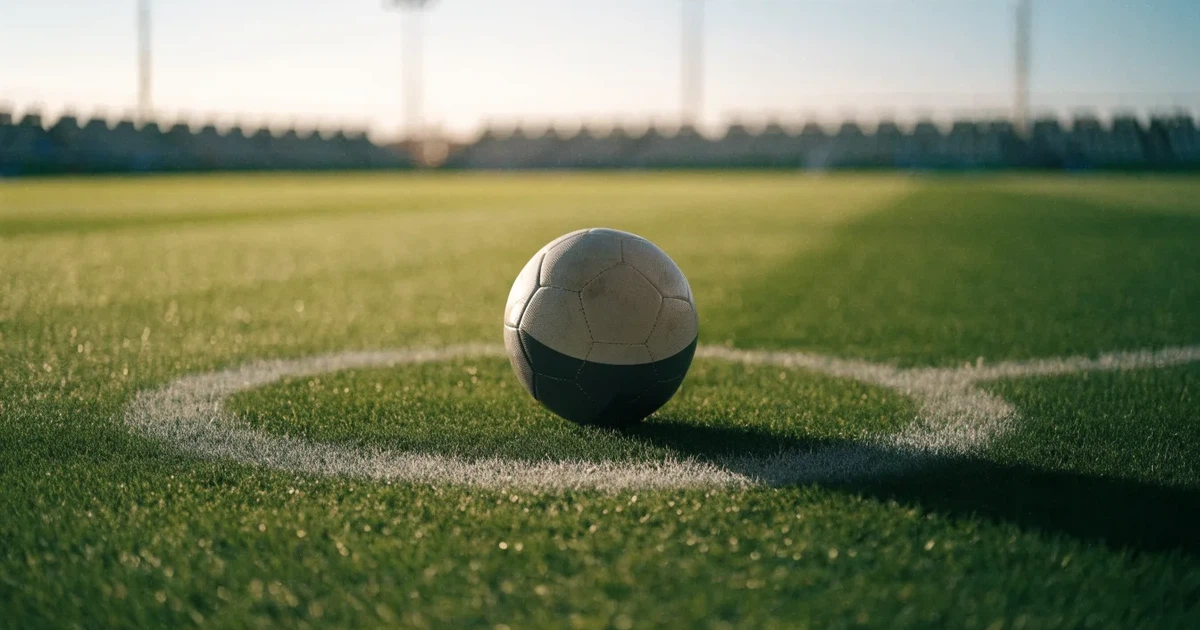Un pallone da calcio sul dischetto del centrocampo di un prato, alla luce del mattino