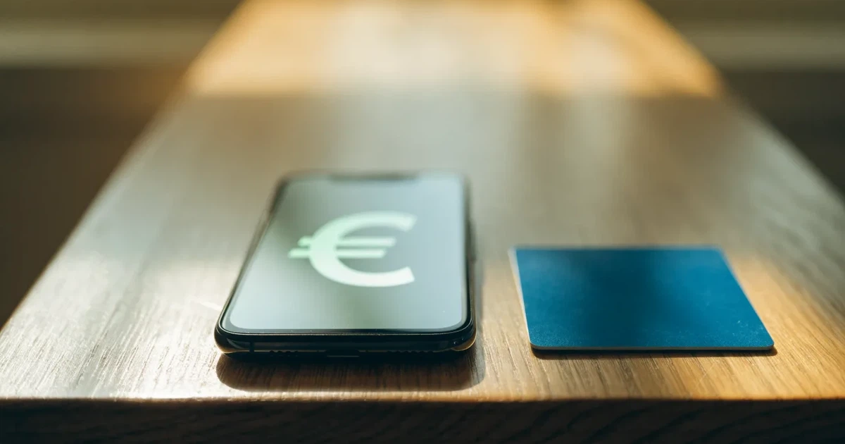Uno smartphone e una carta di pagamento affiancati su un tavolo di legno, con alcune banconote da euro accanto